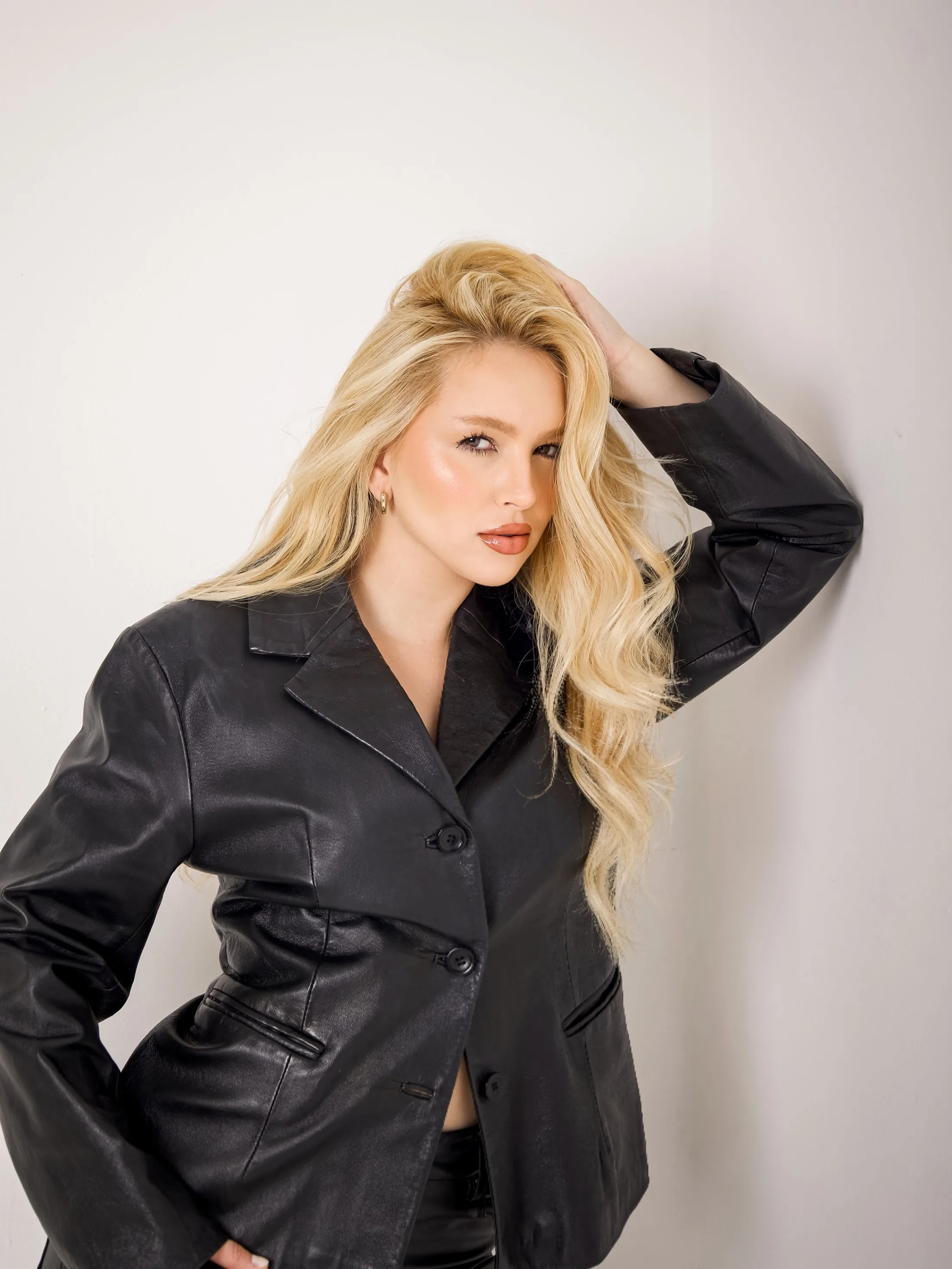 Mulher de blazer preto com a mão nos cabelos, em estúdio.