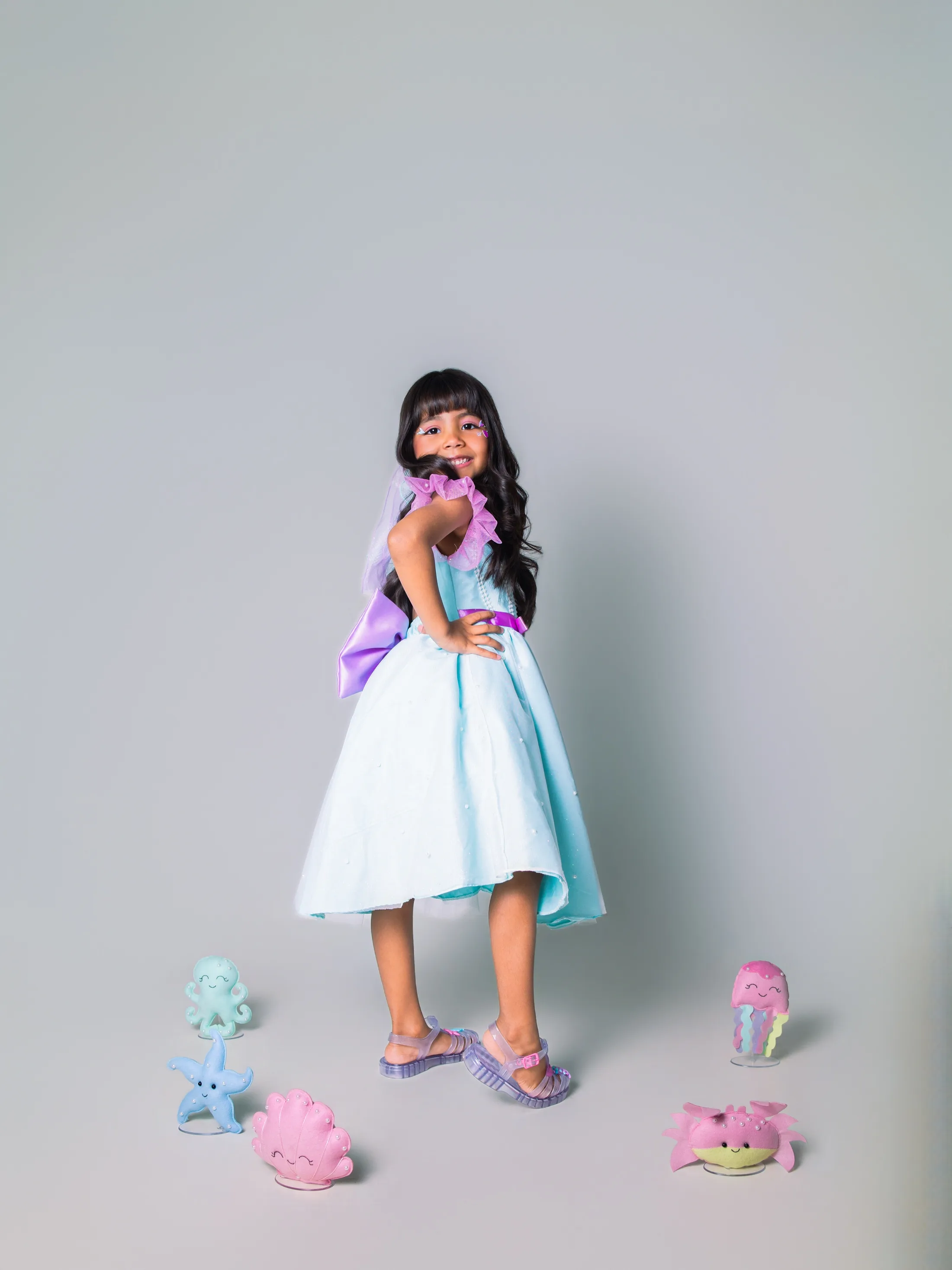 Menina de vestido azul em pé em fundo cinza.