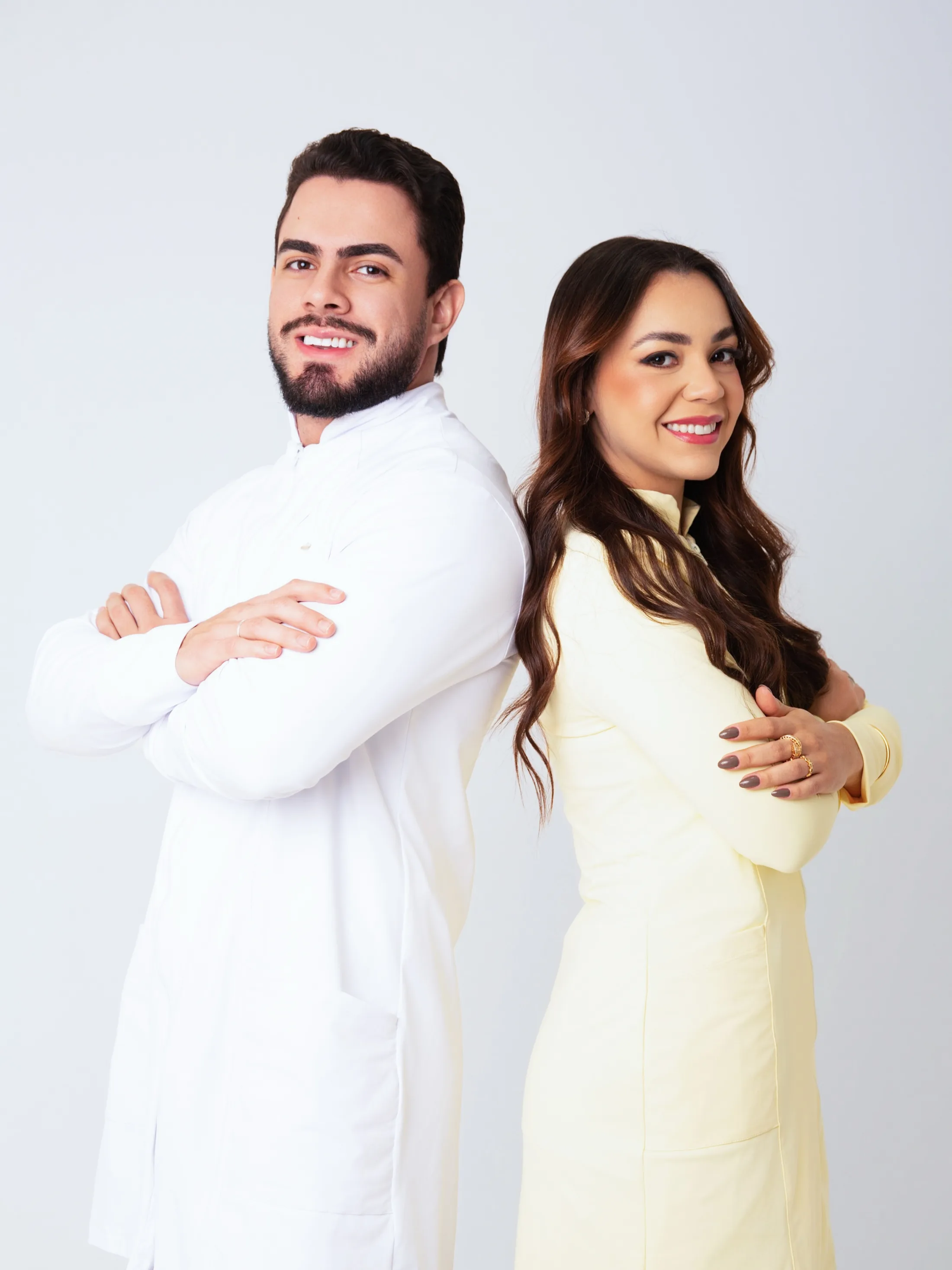 Dupla de profissionais com roupas claras em fundo cinza.