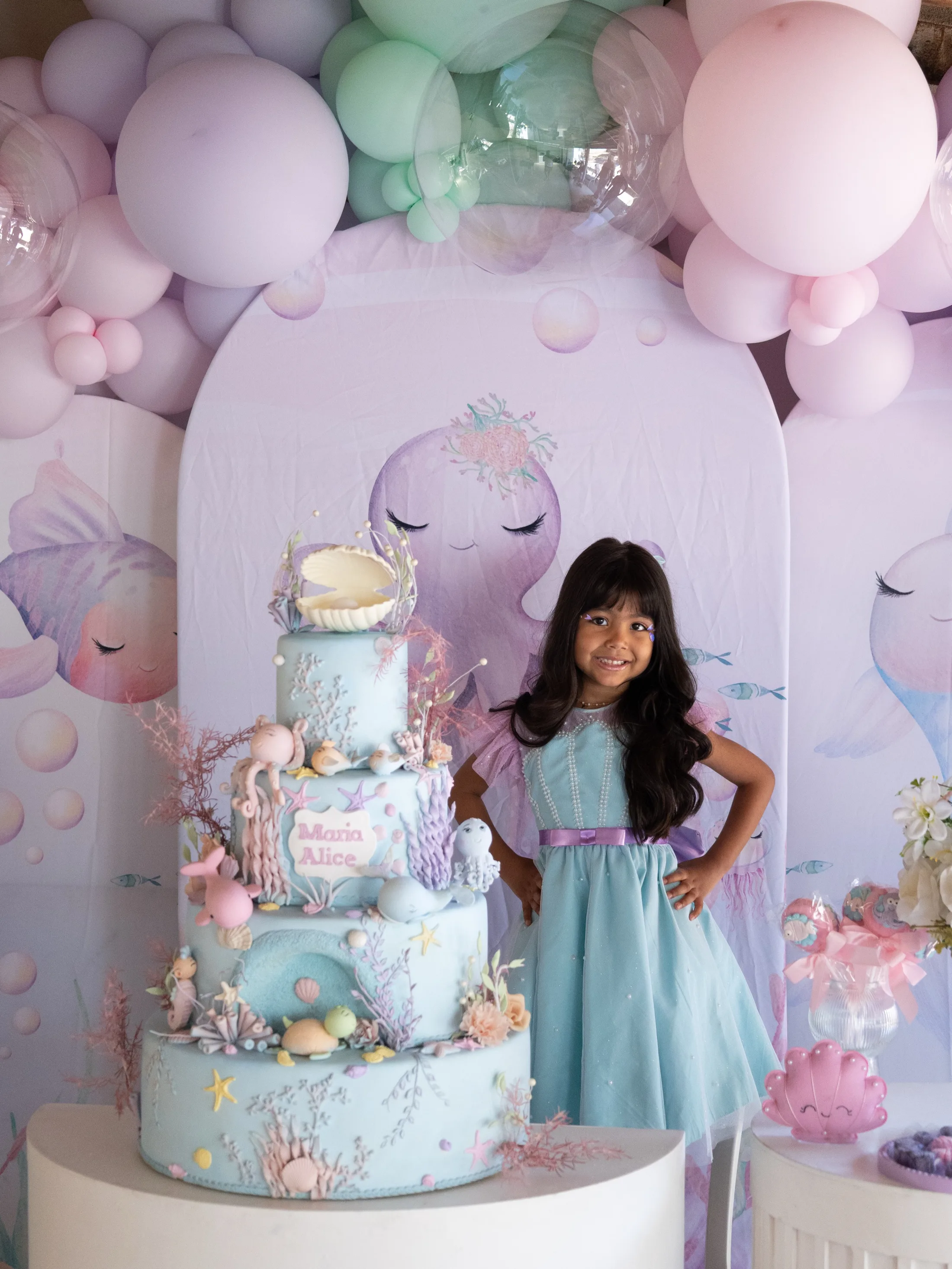 Menina ao lado de bolo e balões de aniversário.