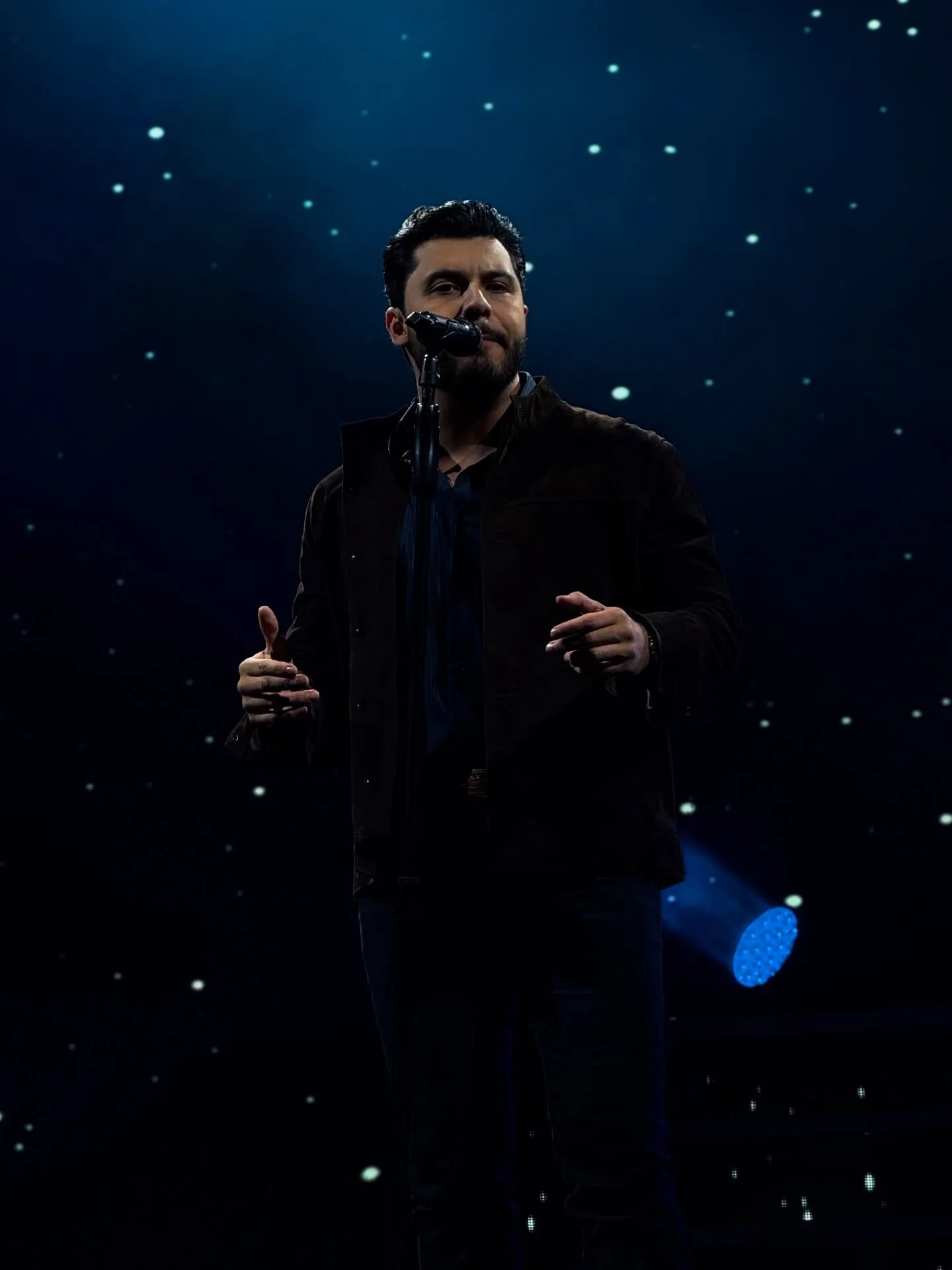 Cantor ao microfone sob iluminação azul no palco.