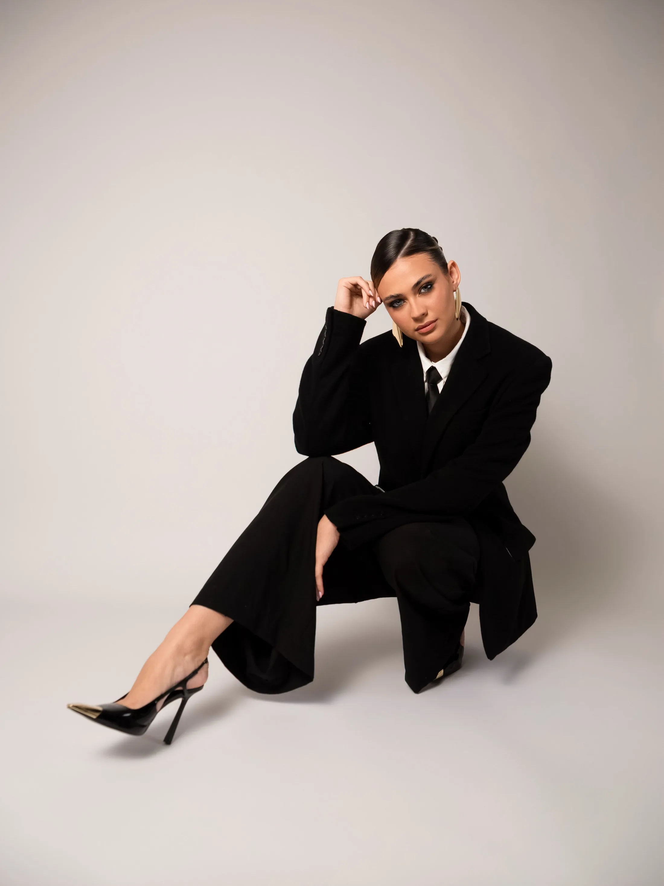 Mulher de terno preto sentada no chão em fundo claro.