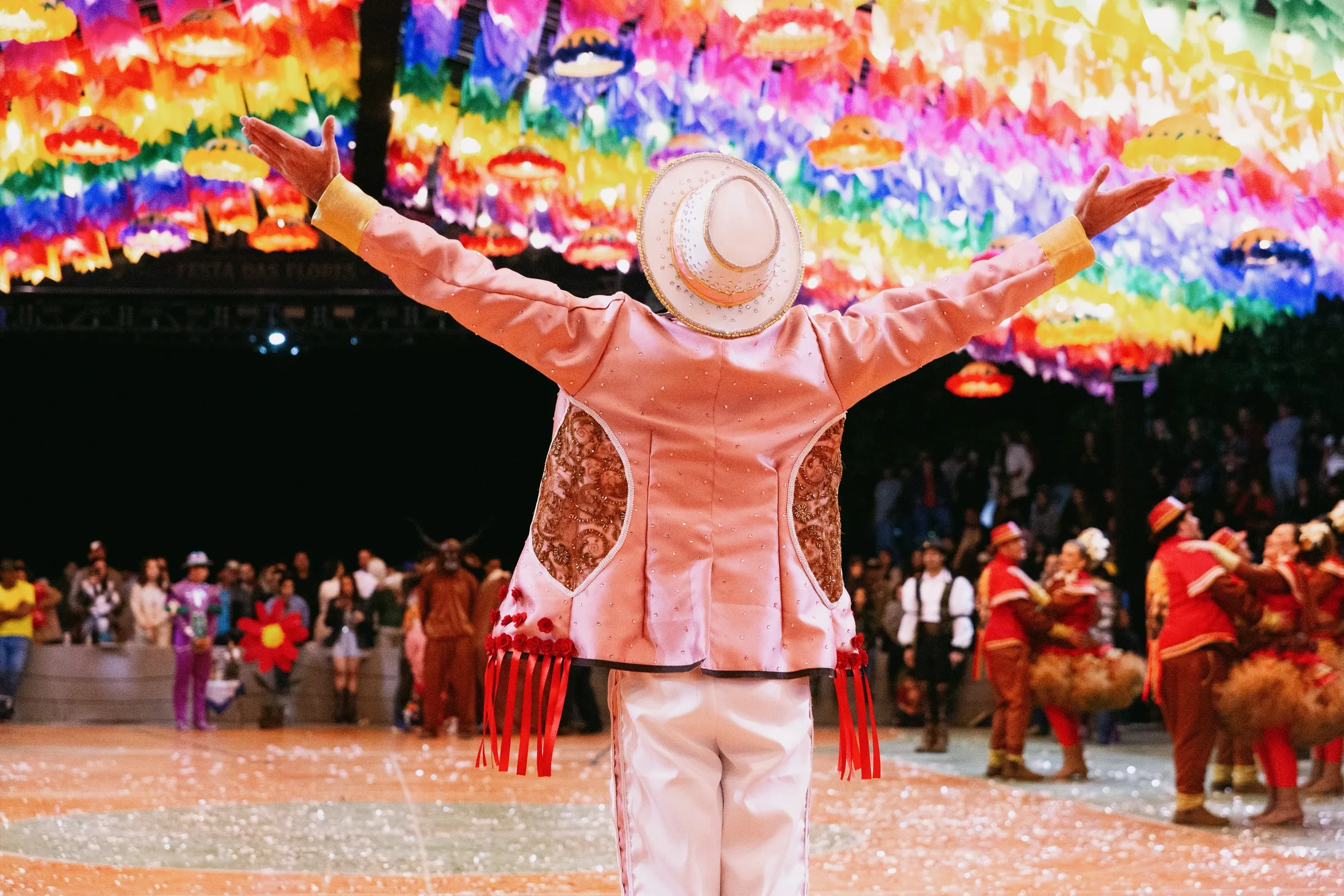 Dançarino de roupa rosa diante de um grupo em apresentação junina.