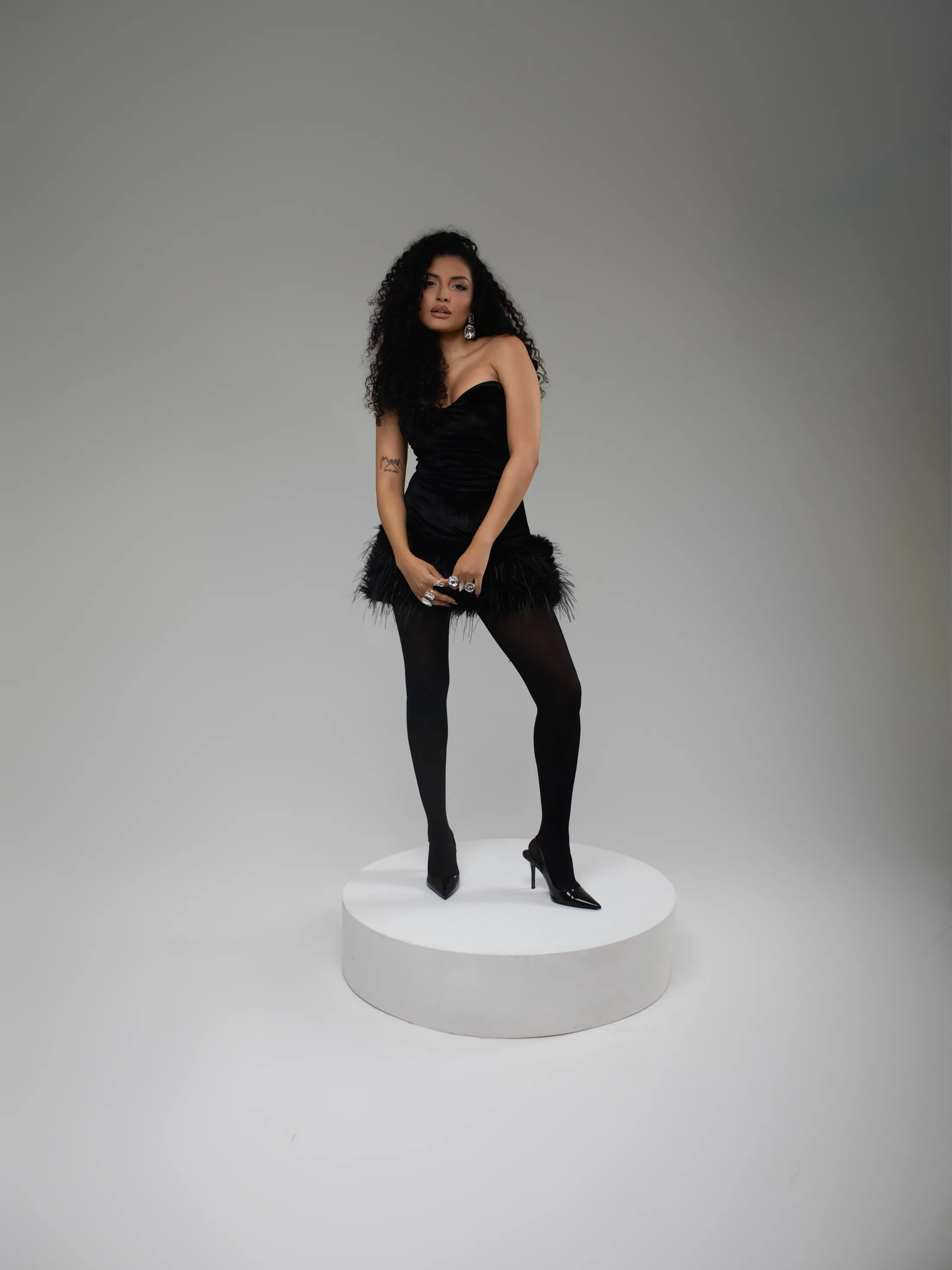 Mulher de roupa preta em pé sobre um cilindro branco.
