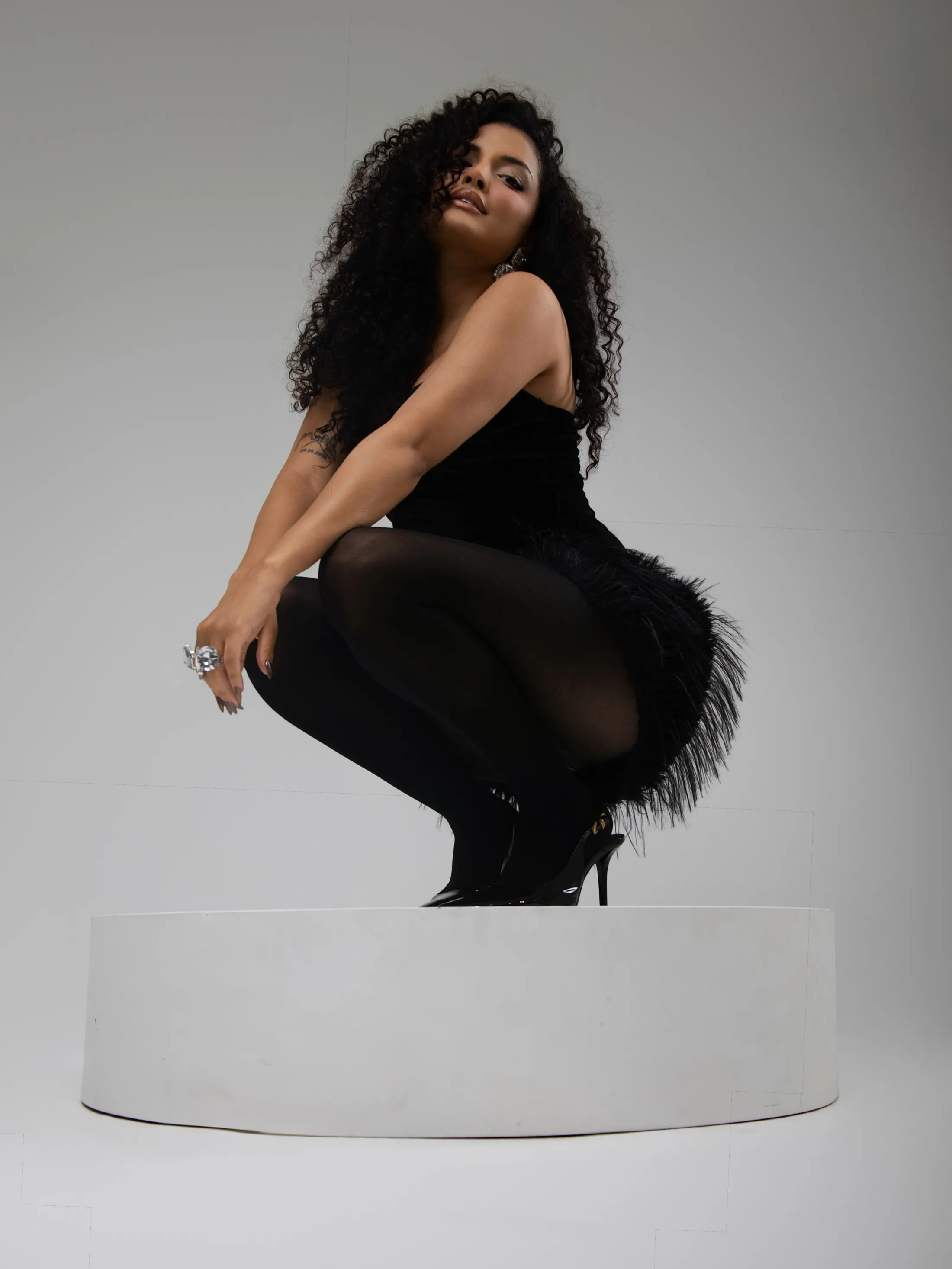 Mulher de roupa preta sentada de lado em um cilindro branco.