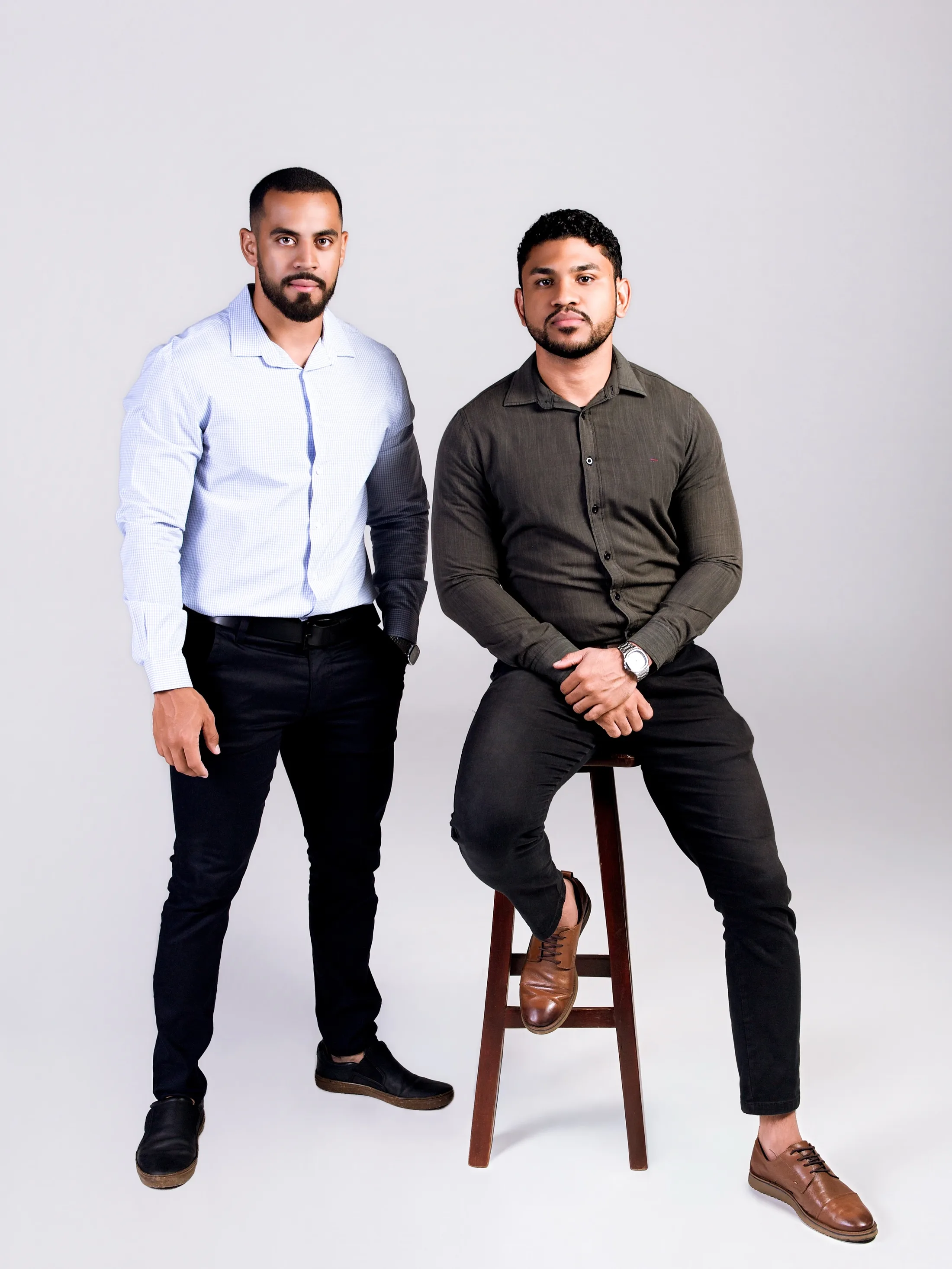 Dois homens, um de camisa clara e outro de camisa escura, em estúdio.