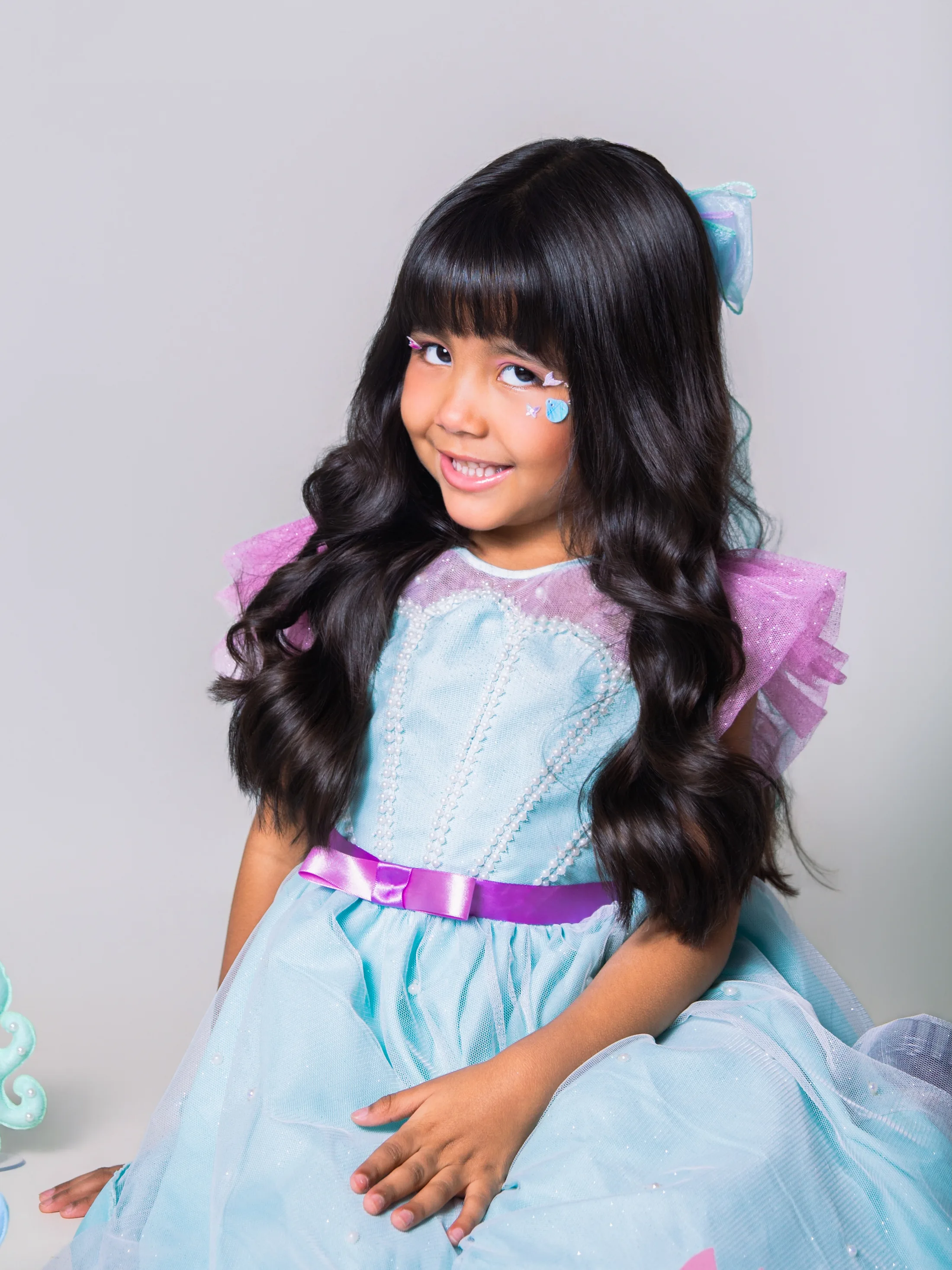 Retrato de menina de vestido azul e roxo sorrindo.