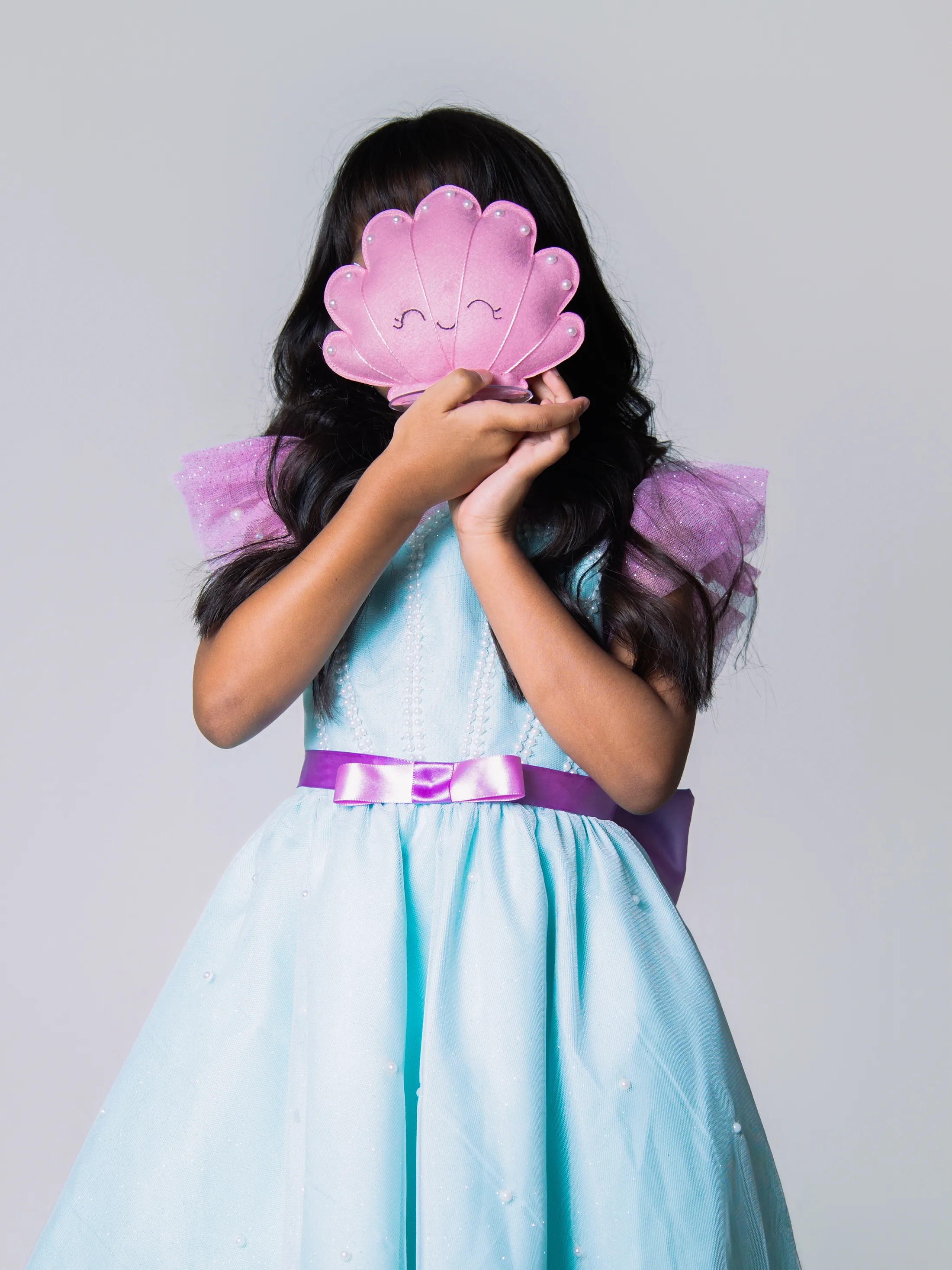 Menina segurando uma concha rosa em frente ao rosto.