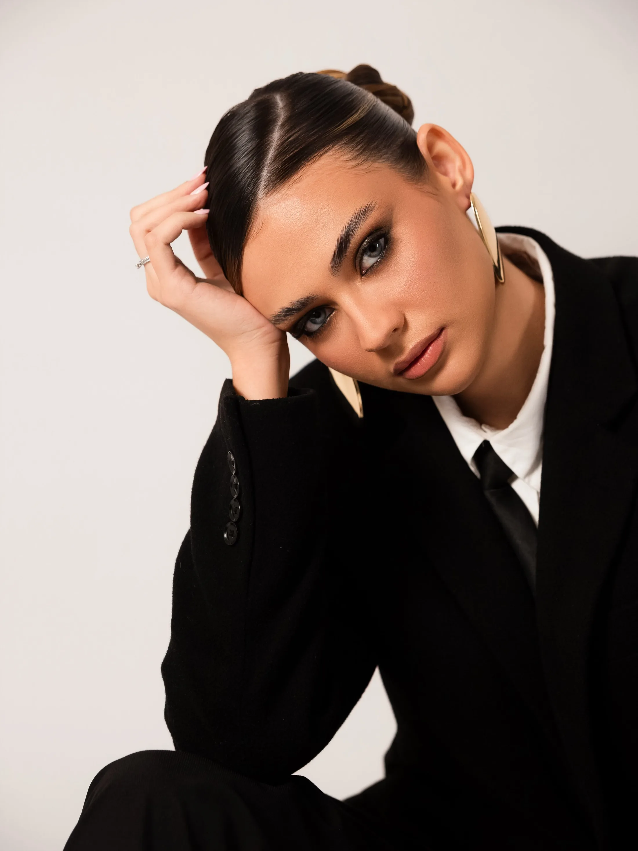 Retrato de mulher de terno preto com a mão apoiada na cabeça.
